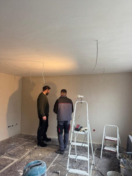 Zwei Arbeiter überprüfen die Decke in einem Raum mit Leitern und Werkzeug.