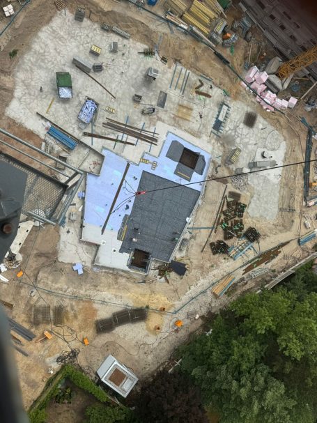Drohnenaufnahme einer Großbaustelle mit vorbereiteter Bodenplatte, Baustellenmaterialien und teilweise verlegter Dämmung – Blick von oben au