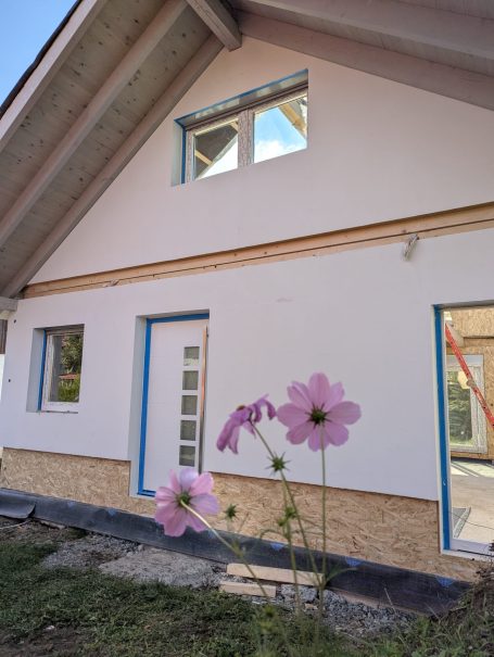 Fertig montiertes Holzhaus mit Putzfassade und Blumen im Eingangsbereich – schlüsselfertiger Neubau in Bayern