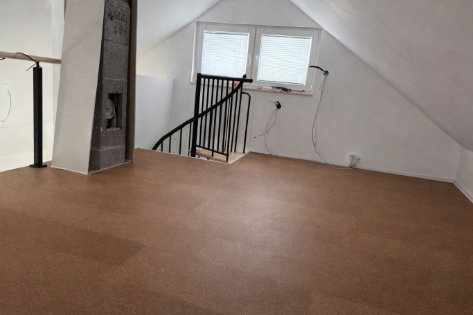 Helle, leere Dachgeschosswohnung mit Fenster und Treppe. Böden sind mit hellem Material ausgelegt.
