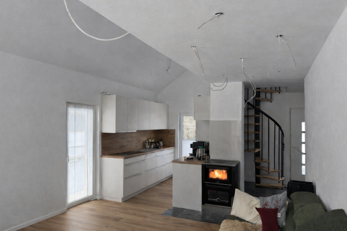 Heller Wohnraum mit Küche, Holzofen und moderner Treppe zu einem oberen Bereich.