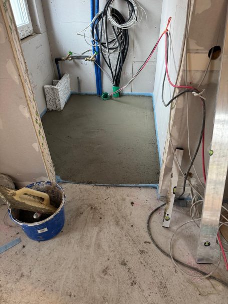 Boden mit frischem Beton in einem Raum, ausgestattet mit Werkzeugen und Kabeln.