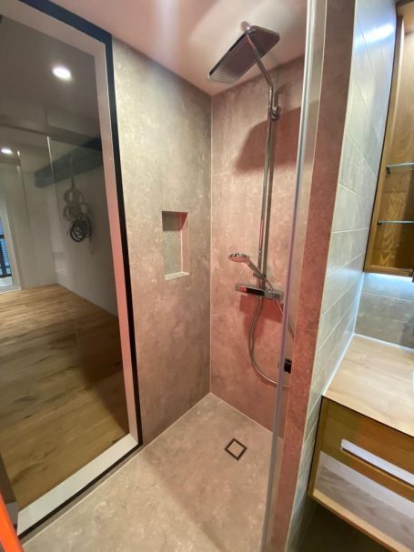 Moderne Dusche mit gläserner Trennwand, Wandregal und Holzboden.
