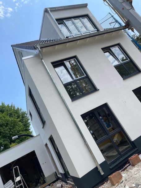 Neues modernes Haus mit weißen Wänden und großen Fenstern, umgeben von Baum und Baugeräten.
