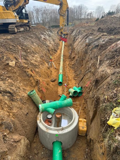 Grabenbau mit grünem Rohr und Betonring für Abwasserinstallation.
