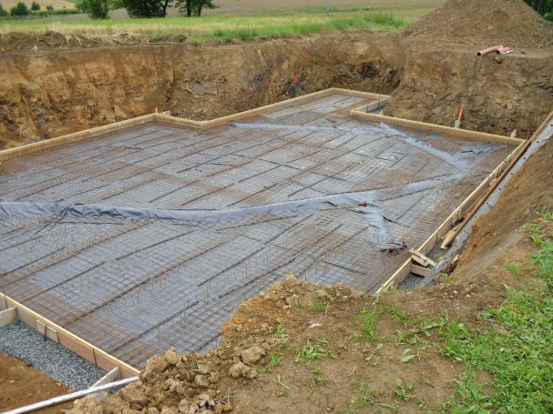 Baugrube mit Betonfundament und Bewehrungsstahl, umgeben von Erdreich.