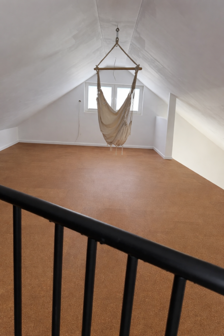 Heller, leerer Raum mit schwingendem Stuhl und Holzboden.