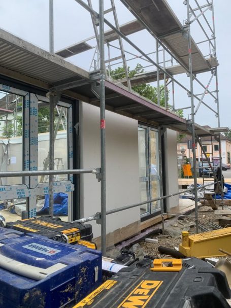 Baugerüst um ein unvollendetes Gebäude mit Baumaterialien im Vordergrund.