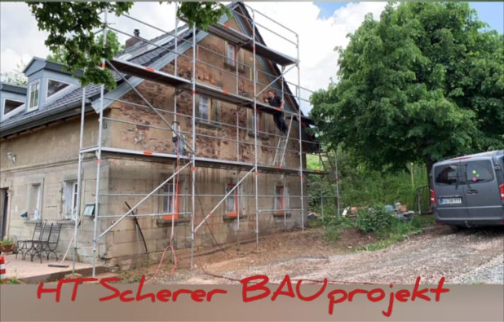 Sanierung eines Hauses mit Gerüst, angrenzendes Auto und Bäume im Hintergrund.