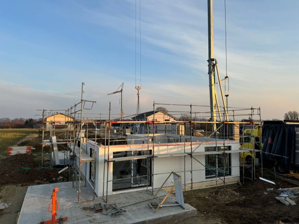 Bau eines modernen Hauses mit Gerüsten und Kranen im Hintergrund.