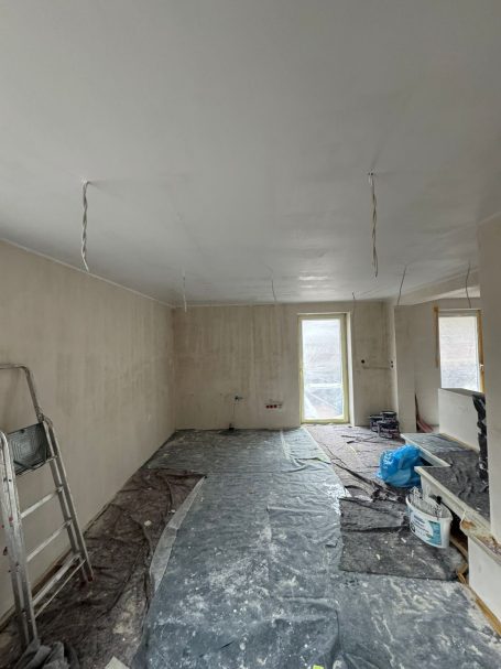 Ein leerer Raum mit unvollendeten Wänden und Sicht auf ein Fenster. Boden mit Folie abgedeckt.