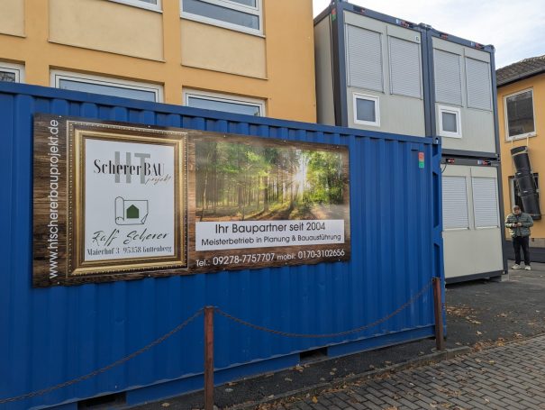 Bauschild von HT Scherer BAUprojekt vor blauen Containern – Ankündigung eines neuen Bauprojekts“