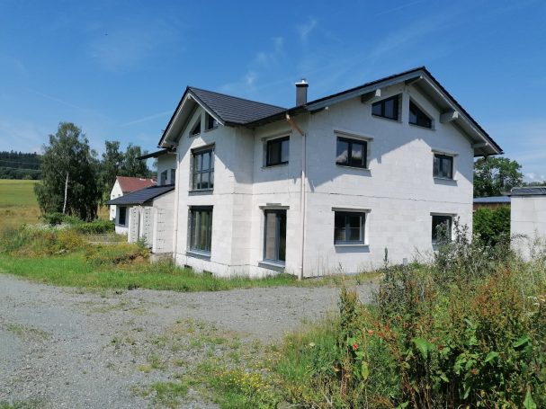 Zweistöckiges, helles Wohnhaus umgeben von Wiesen und Bäumen.