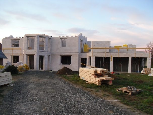 Rohbau eines modernen Hauses mit Baustellenmaterial im Vordergrund.