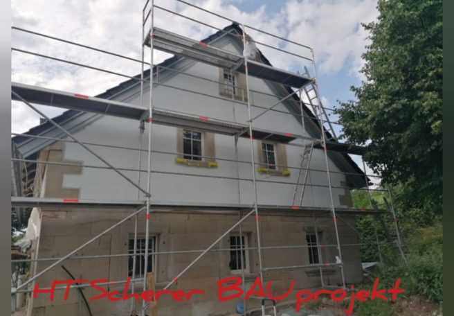 Haus mit Gerüst für Bauarbeiten umgeben von Bäumen.