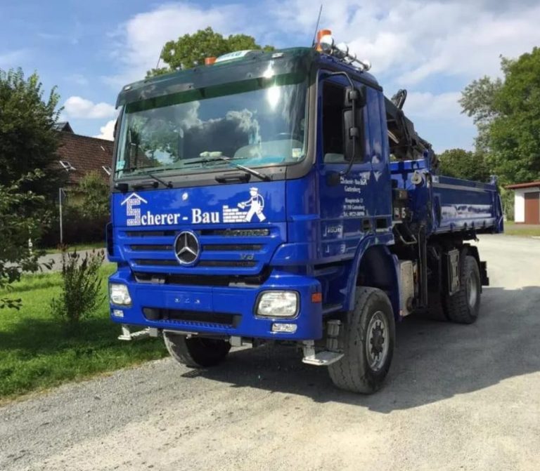 Blauer Mercedes-Lkw mit Aufschrift auf der Fahrzeugseite, fahrend auf einer gravel Straße.