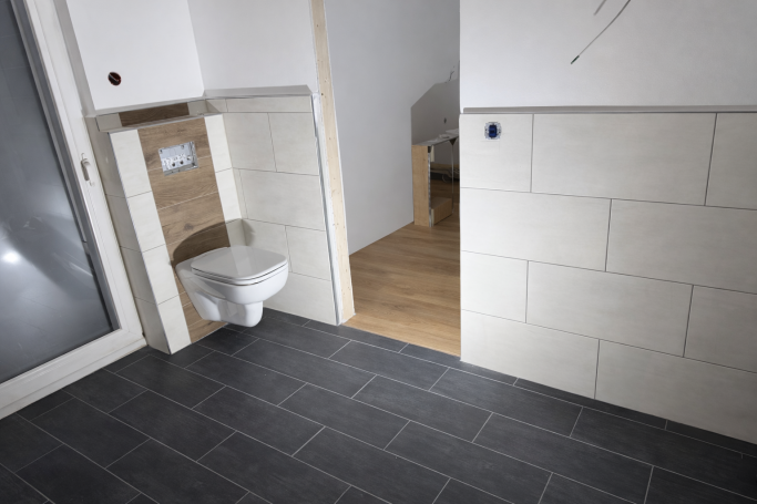 Badezimmer mit Toilette, Fliesenboden und einem offenen Raum im Hintergrund.