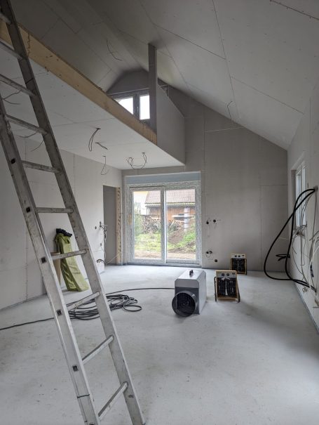 Innenraum eines im Bau befindlichen Hauses mit montierten Trockenbauwänden, Leiter, Werkzeugen und großem Fenster nach außen