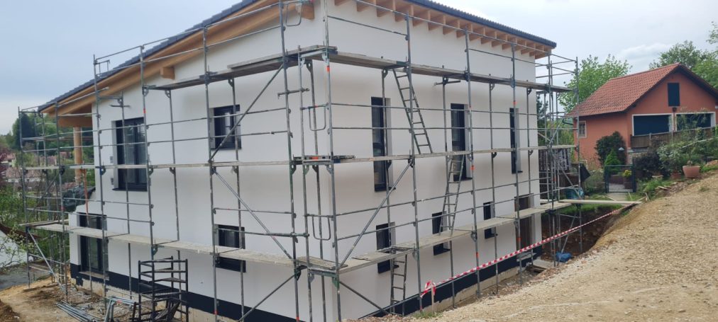 Haus im Bau mit Gerüst, weißen Wänden und angrenzendem Gelände.