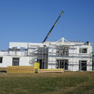 Rohbau eines Einfamilienhauses in Ytong-Massivbauweise mit Baukran, Gerüst und vorbereiteten Holzbalken für den Dachstuhl – Neubauprojekt