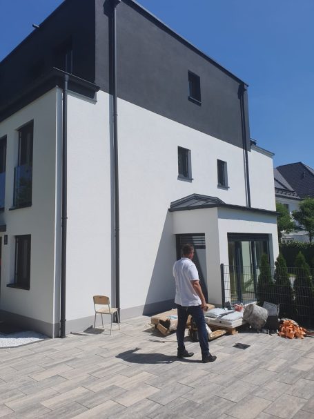 Moderne Hausfassade mit blauer Fassade und Terrasse, Bauarbeiten im Vordergrund.
