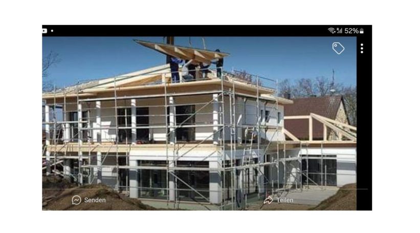 Rohbau eines Hauses mit Bauarbeitern auf dem Dach und Gerüst um das Gebäude.